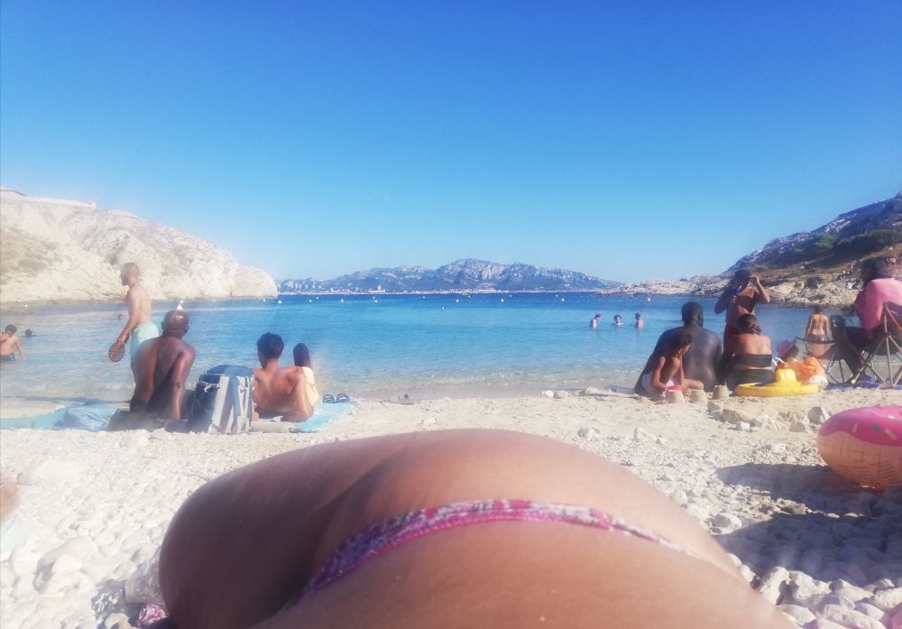 .photo d'un bas de corps heureux en maillot qui bronze paisiblement sur la plage. en second plan des gens , en troisième la mer.
