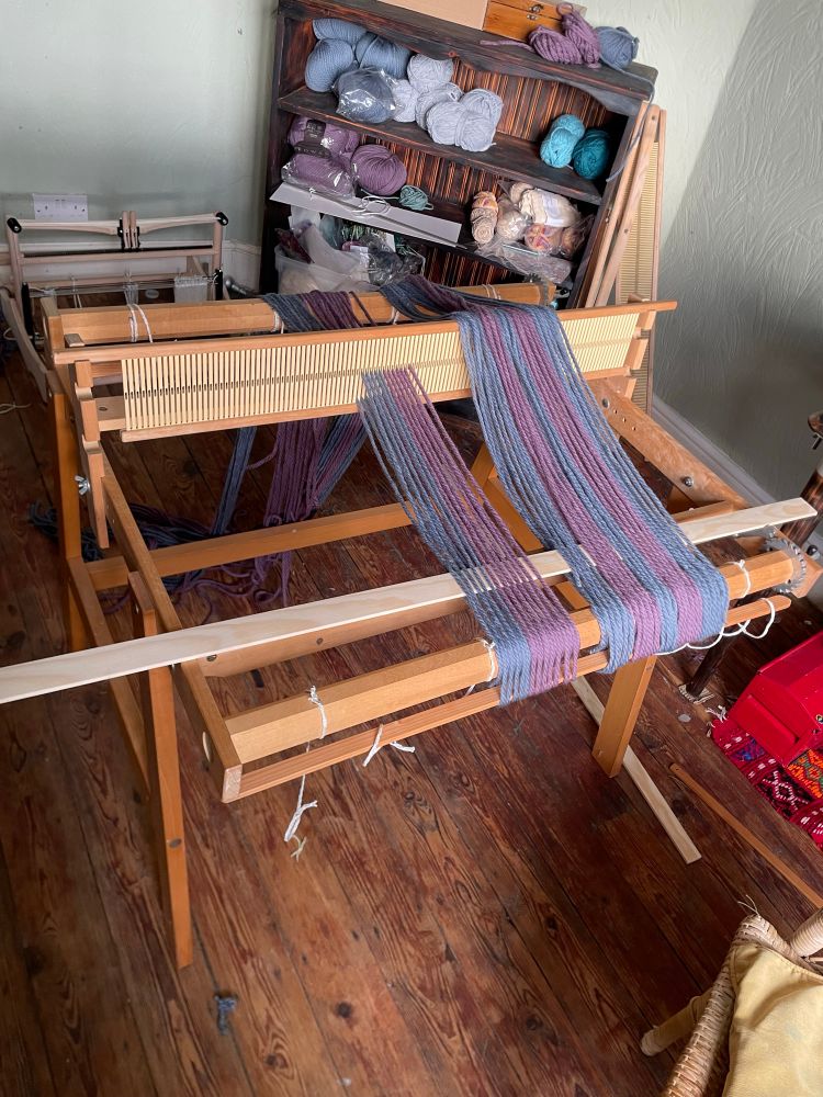 A rigid heddle loom, going under a slow warping process, with two tones of wool, in baby blue and mauve/magenta. 