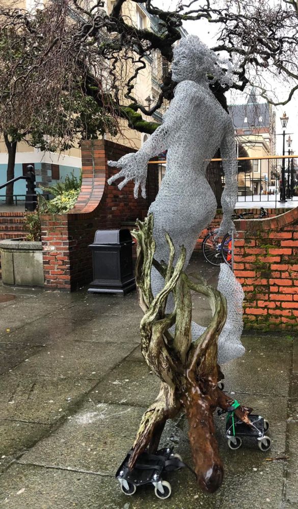 The photo shows a mermaid statue made of chicken wire & driftwood