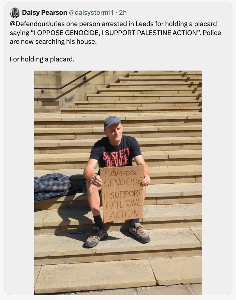 Person sitting on steps and holding a placard saying "I OPPOSE GENOCIDE, I SUPPORT PALESTINE ACTION"