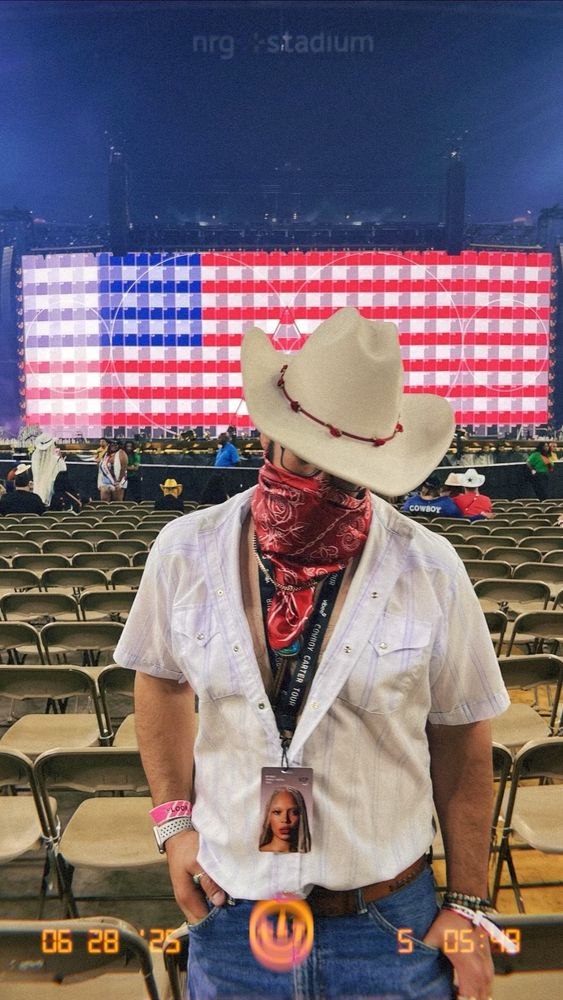 I’m standing in front of an electronic display screen broadcasting a digital American flag. I’m wearing a white cowboy hat, a red bandana pulled over my mouth, a white cowboy tee unbuttoned, and denim shorts.