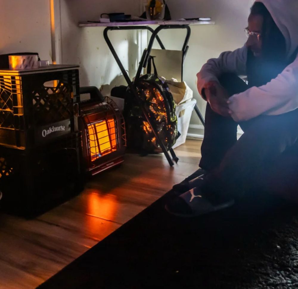 A man hunches on the floor in front of a space heater inside an apartment