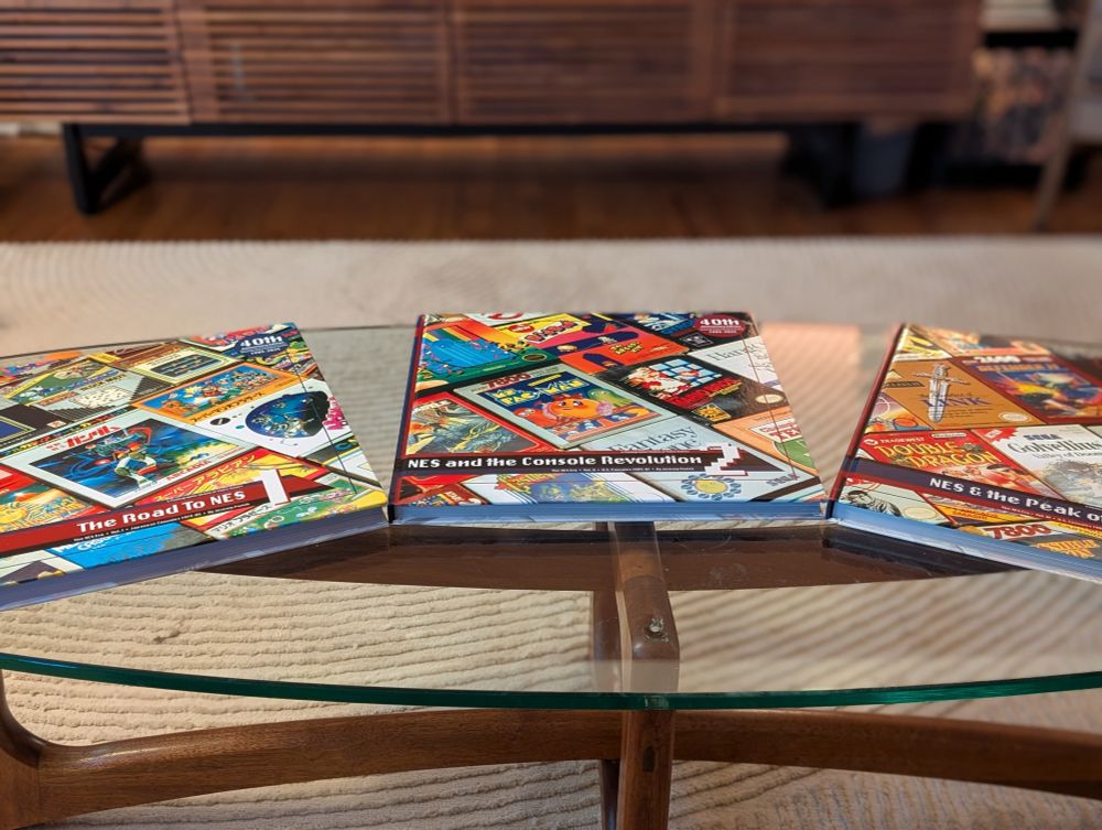 Three coffee table books about the NES era written by Jeremy Parish sitting on a glass coffee table