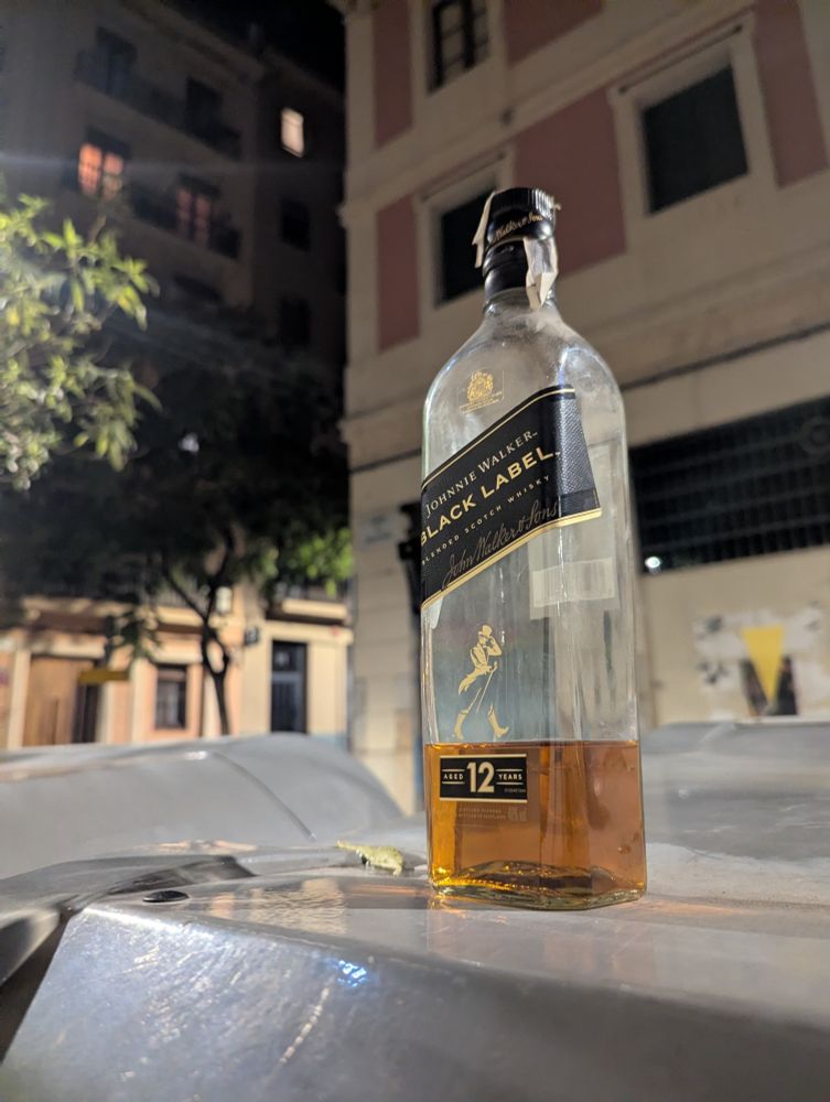 At night, on a quiet street, atop a garbage bin, a bottle of scotch