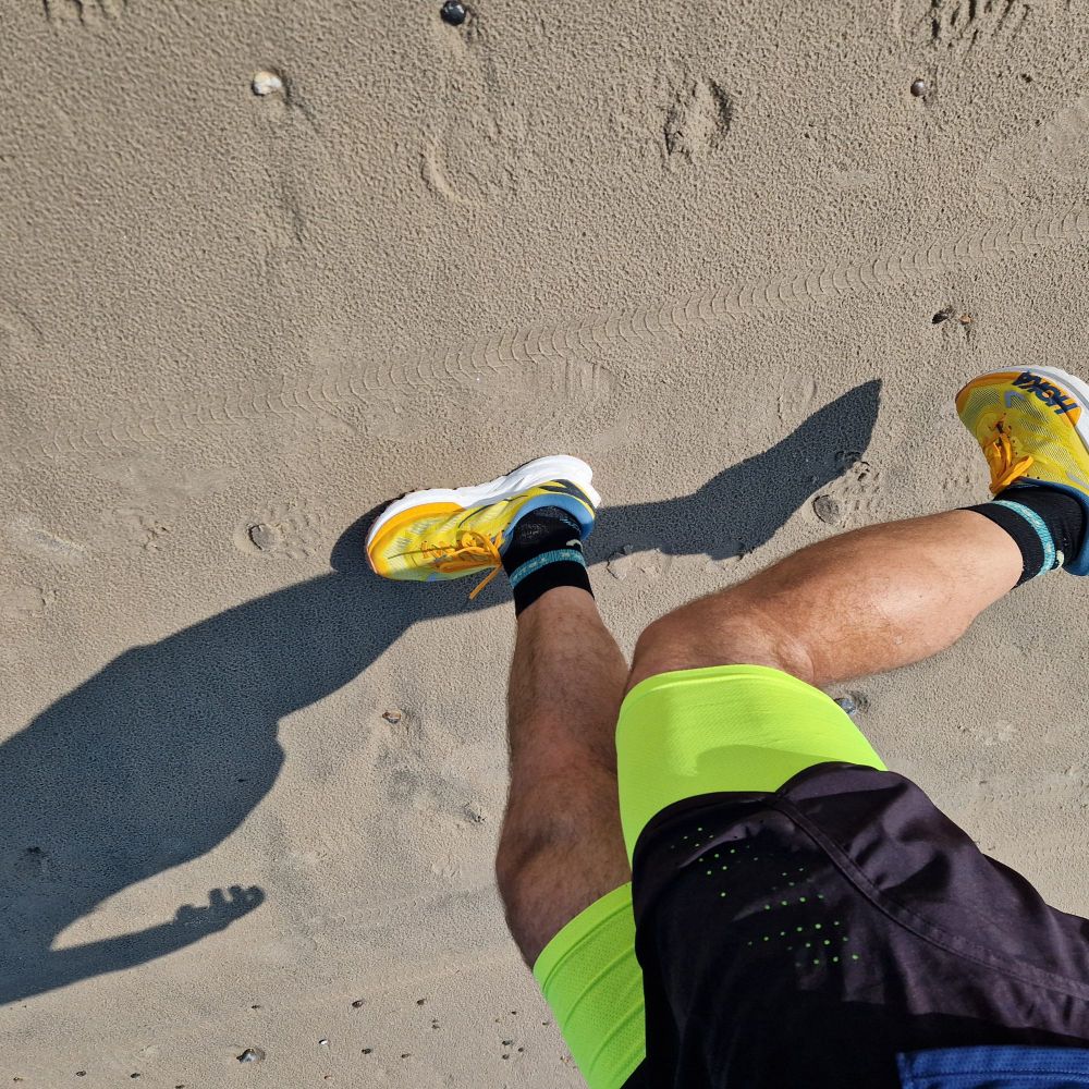Die Beine eines Läufers von oben fotografiert,  während er über nassen Sand läuft