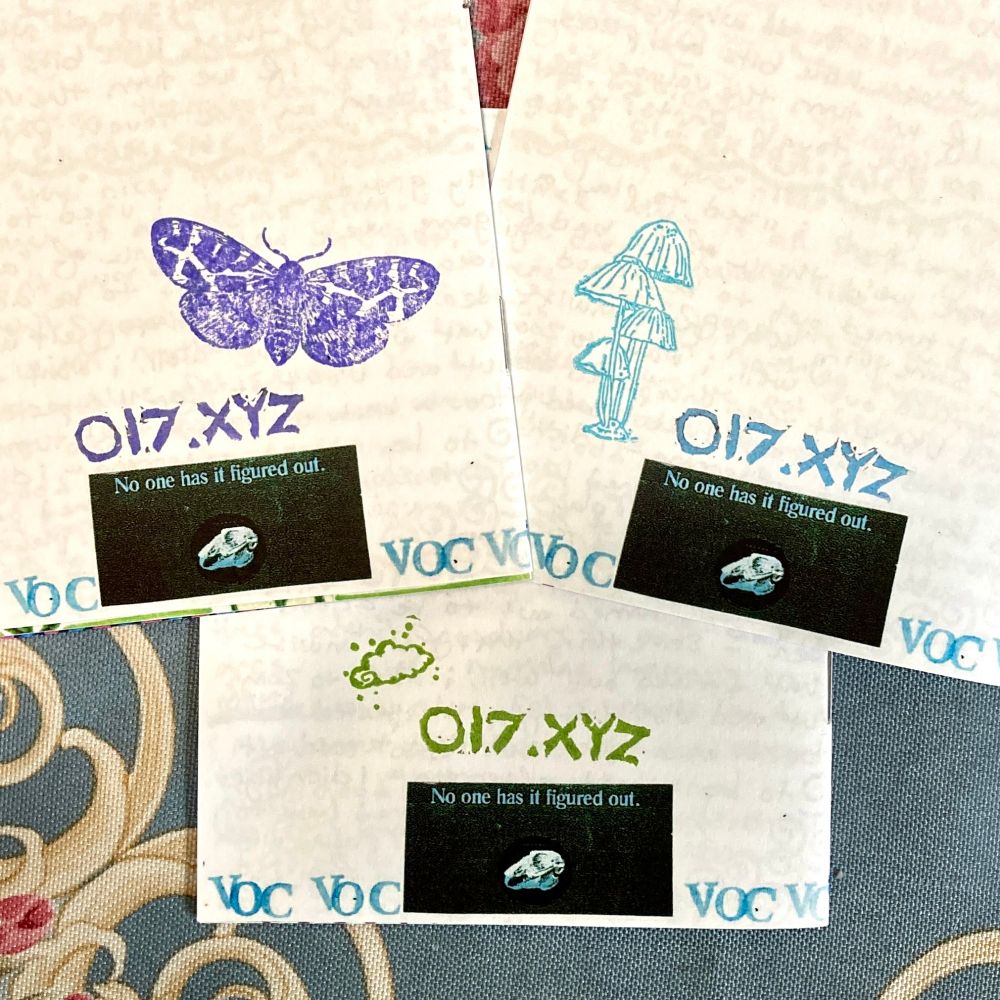 the back of three zines, showing a screenshot from the app co-star that says "no one has it figured out" with a rabbit skull under it. each has a stamp that reads "o17.xyz" and a different accompanying image - a purple moth, blue mushrooms, and a green cloud.