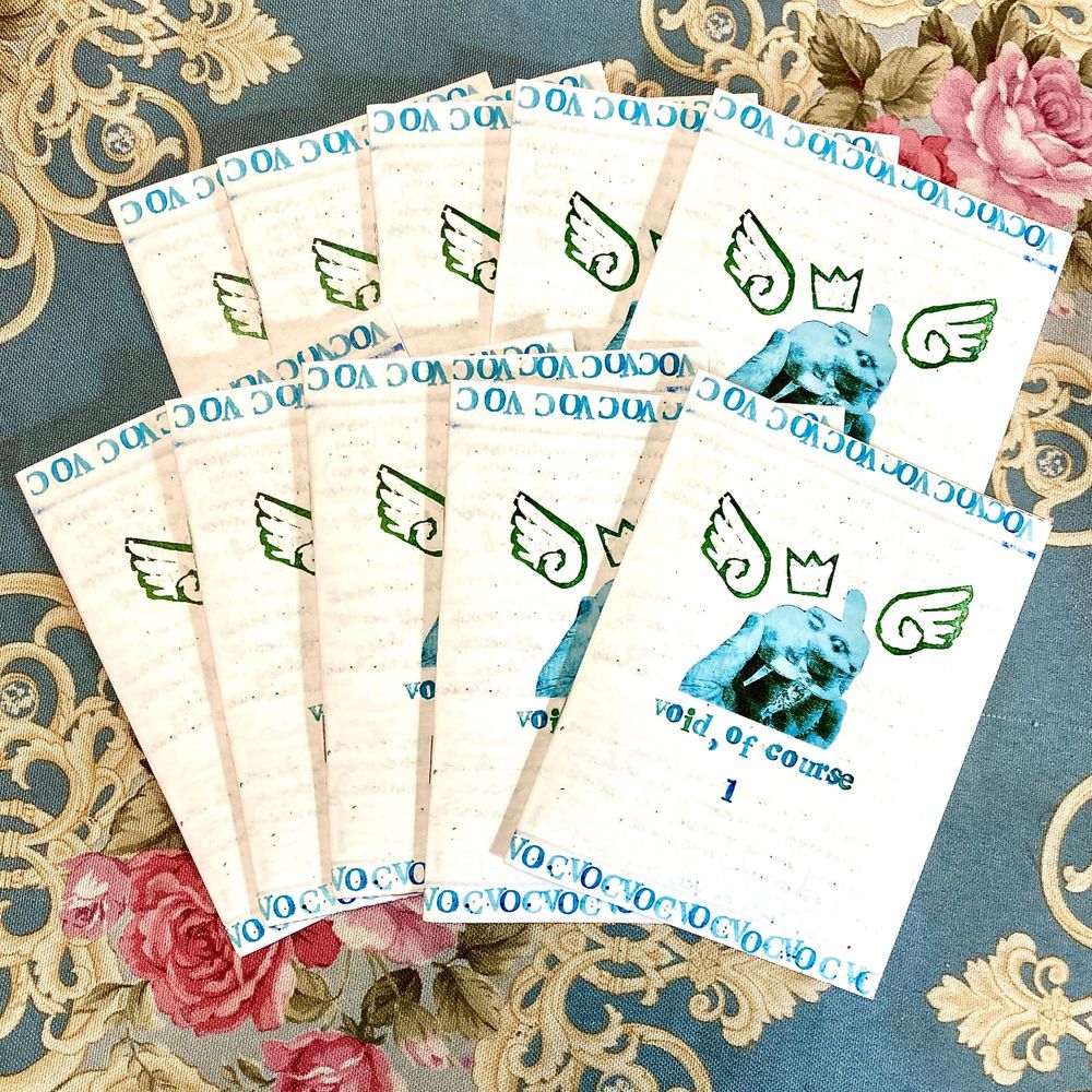 a stack of ten zines, five behind and five in front. all of the text is printed in blue with hand stamped letters. the top and the bottom edges of the zine are lined with "VOC" repeated over and over again. in the middle is a blue sticker of a hand holding up a porcelain bunny statue. there are block printed wings and a crown around the bunny, and under it, the zine's title - "void, of course 1".