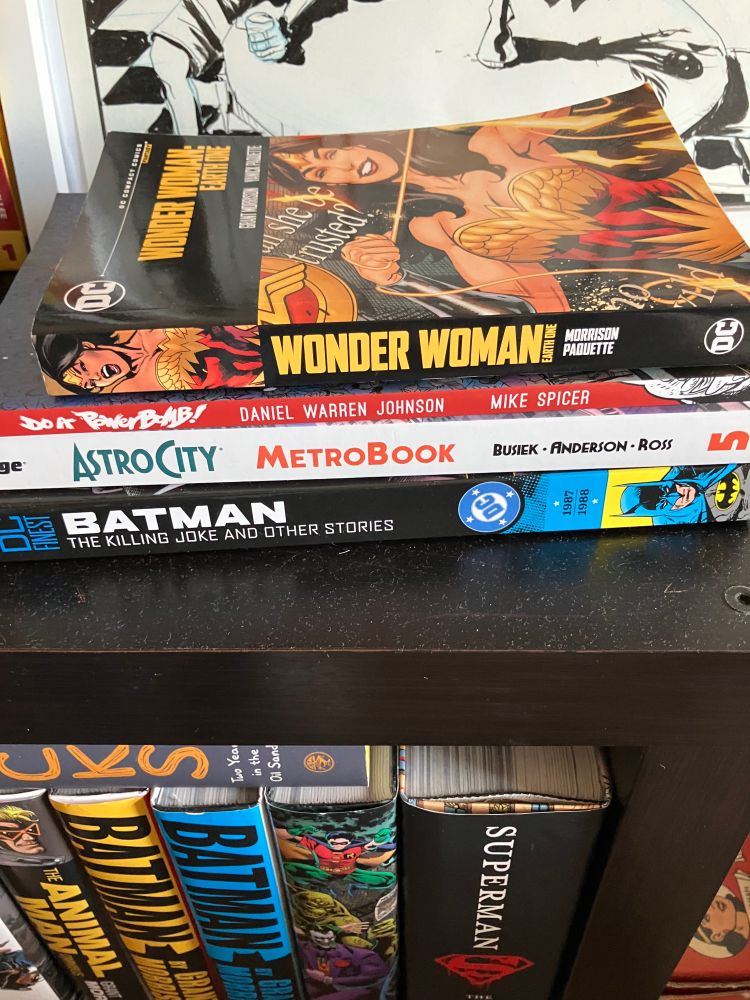 Stack of trade paper backs 
Wonder Woman earth one compact edition
Do a power bomb
Astrocity metro book volume 5
Batman the killing joke and other stories 