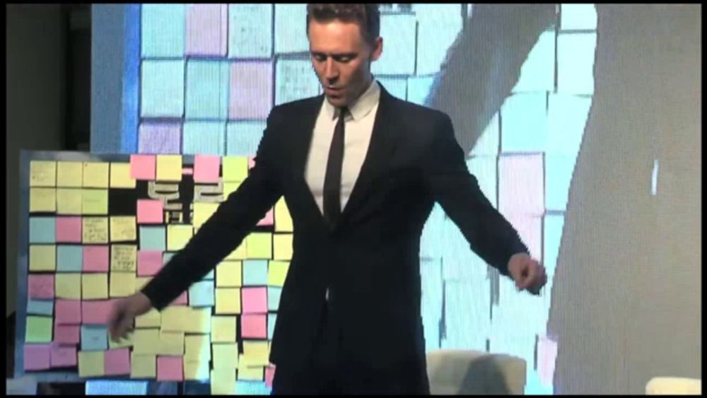 a man in a suit and tie is standing in front of a wall of sticky notes