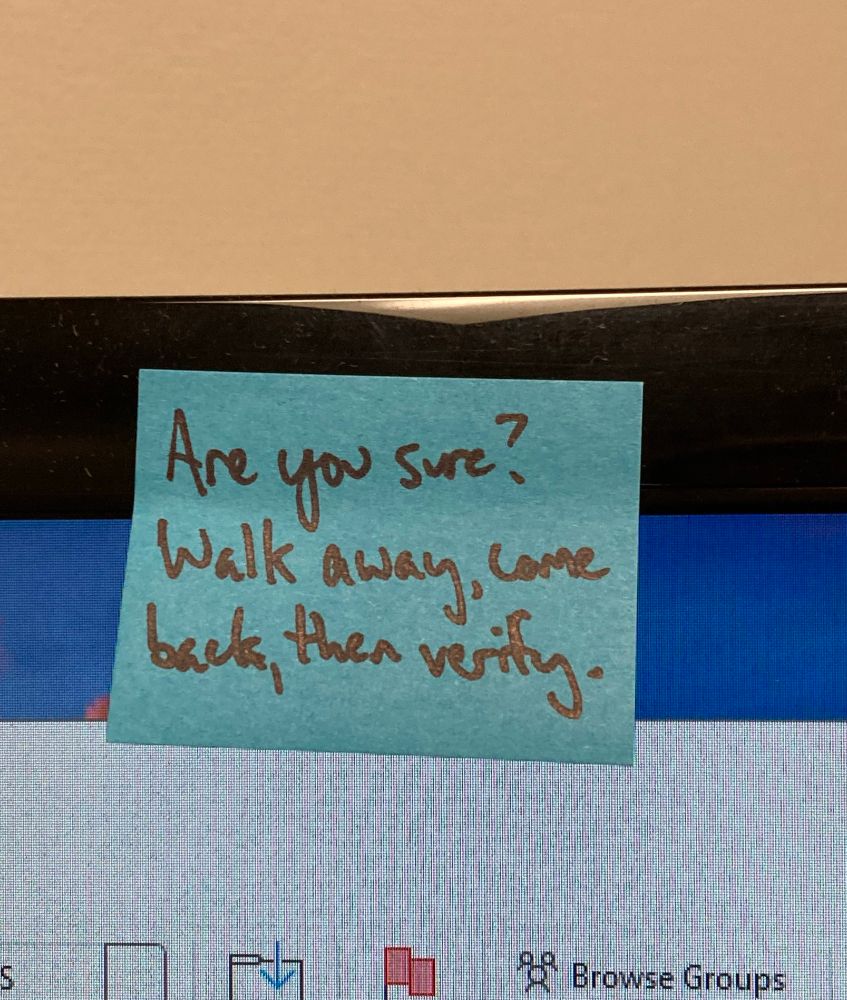 A bright blue mini sticky note on the top bezel of a monitor. Written on it in black marker is the admonishment “Are you sure? Walk away, come back, then verify.” 
The few square inches of visible computer screen contain some Outlook toolbar buttons.