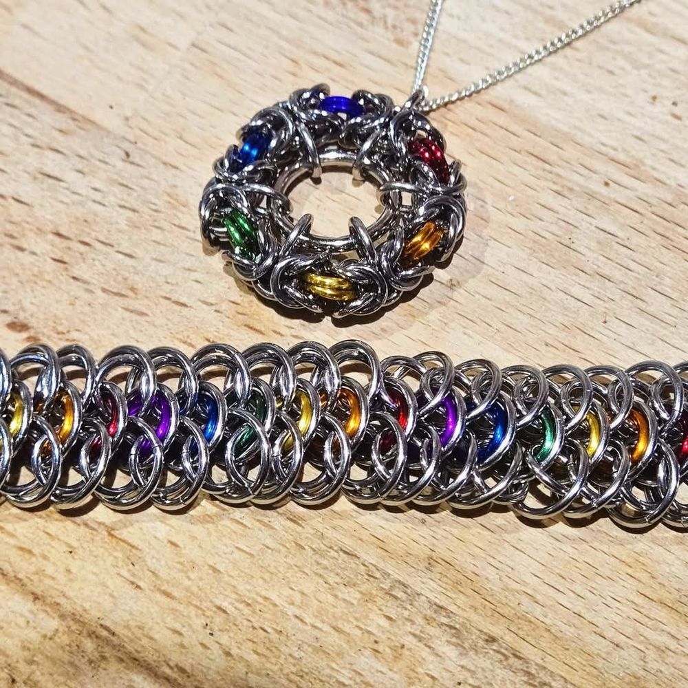A circular pendant in byzantine and bracelet in affena made in stainless steel with pride rainbow coloured anodised aluminium accents.