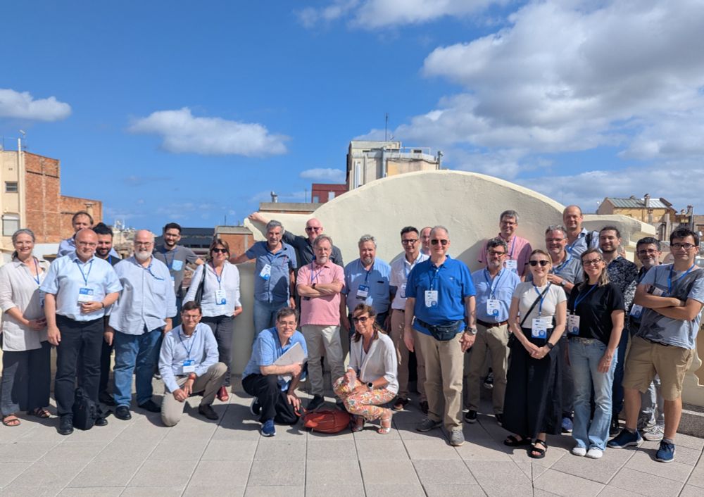A group photo of ET-PP Annual Meeting participants taken on the rooftop terrace under a bright blue sky. The attendees, wearing conference badges, are standing and smiling against a backdrop of city buildings.