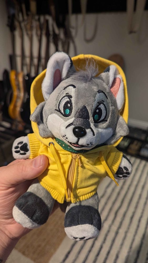 small plush gray fox in a yellow hoodie with green eyes and a green collar.