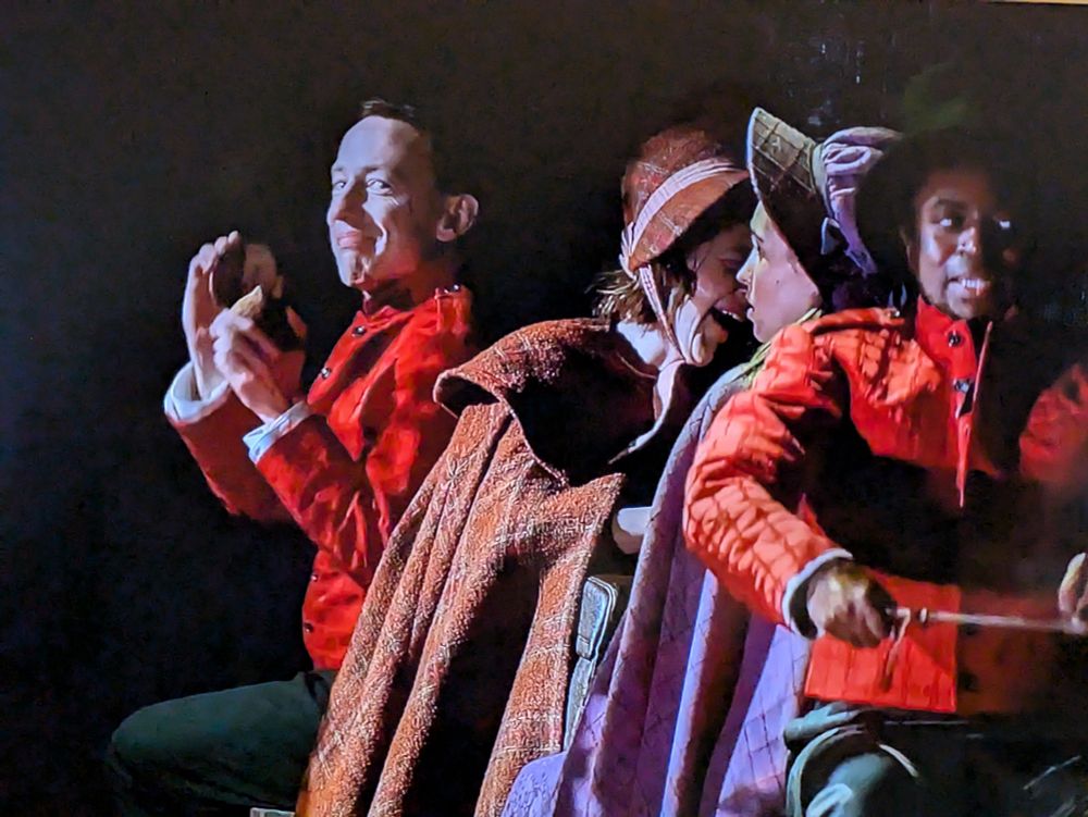 2 female characters in old style travelling clothes, with a driver in front managing hypothetical horses and a man at the back with coconut shells making clip clip noises and looking very proud of himself.