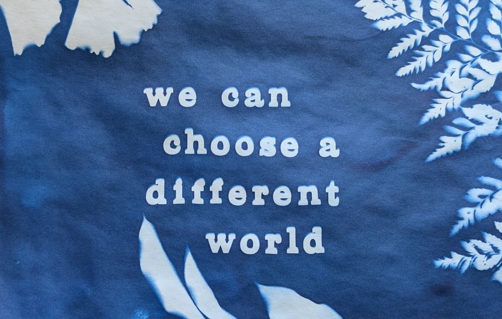 A dark blue background with the silhouettes of gingko leaves and a fern and the words 'we can choose a different world' in white letters.