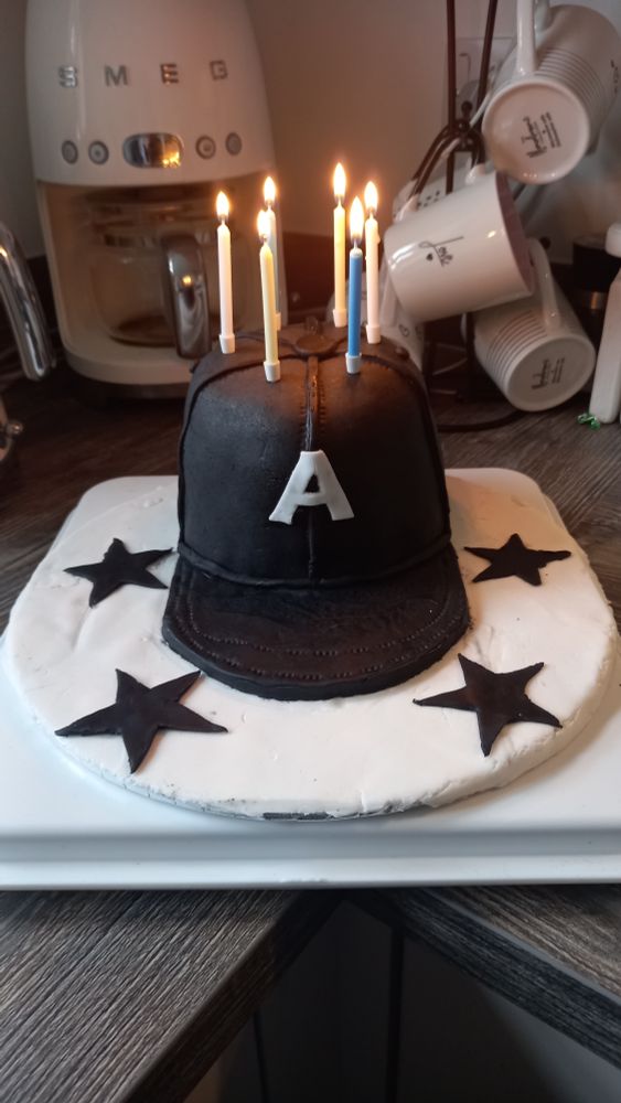 Front view of the cake with candles lit, there is stitching and seams on it