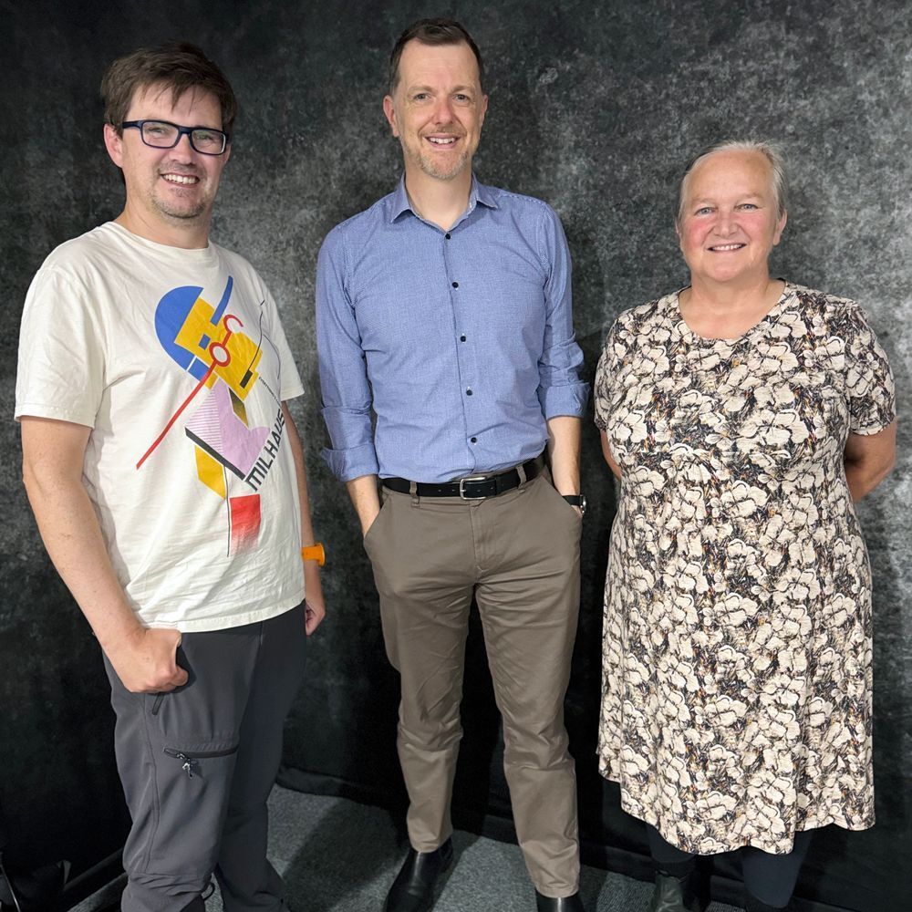 Paul Turner, Jim Wild and Jan Bebbington standing against what looks like a thickly carpeted grey wall! 