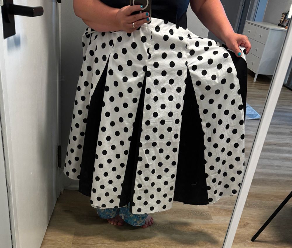 Person holding a black and white polka dot skirt up to show black godets.
