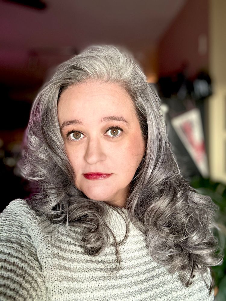 Selfie of woman wearing a grey sweater and has grey/silver hair. 