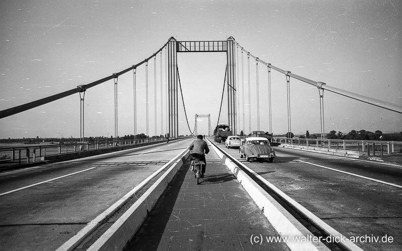 Foto: Walter Dick Auf dem Mittelstreifen hat Walter Dick diese Aufnahme der Rodenkirchener Autobahnbrücke gemacht. Die Brücke war bereits vor dem Krieg als reine Autobahnbrücke geplant und  bis in den Krieg hinein fertiggestellt worden. Das Bauwerk wurde nach Plänen des genialen Brückenbaukonstrukteurs Fritz Leonhardt (1909-1999) und des Architekten Paul Bonatz (1877-1956) erstellt und im September 1941 eröffnet. Nach mehrfachen Bombentreffern stürzte die Hängebrücke Ende Januar 1945 ein. Die Pylone und Widerlager blieben erhalten. Nach dem Krieg wurde die Brücke in der alten Form und Nutzung der erhaltenen Bauteile neu errichtet und im Dezember 1954 dem Verkehr übergeben. (Bauzeit in der sicher schwierigen Nachkriegszeit: zwei Jahre!) Von Anfang an als reine Autobahnbrücke geplant verfügte sie über zwei Richtungsfahrbahnen, zwischen denen ein schmaler, abenteuerlicher Radweg (Anmerkung dazu: siehe unten)verlief und über Fußgängerstege auf beiden Seiten.