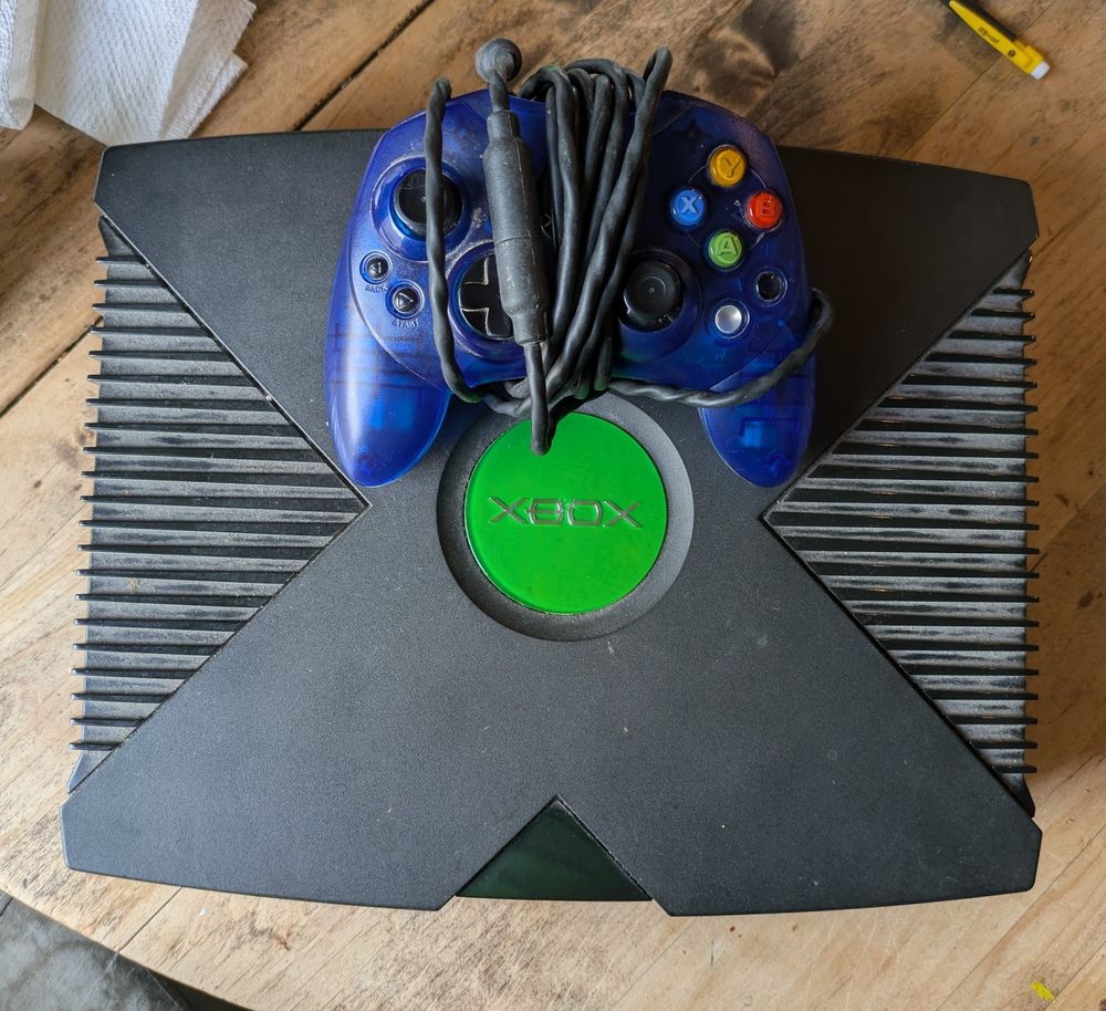 An original Xbox with a blue controller sitting on top