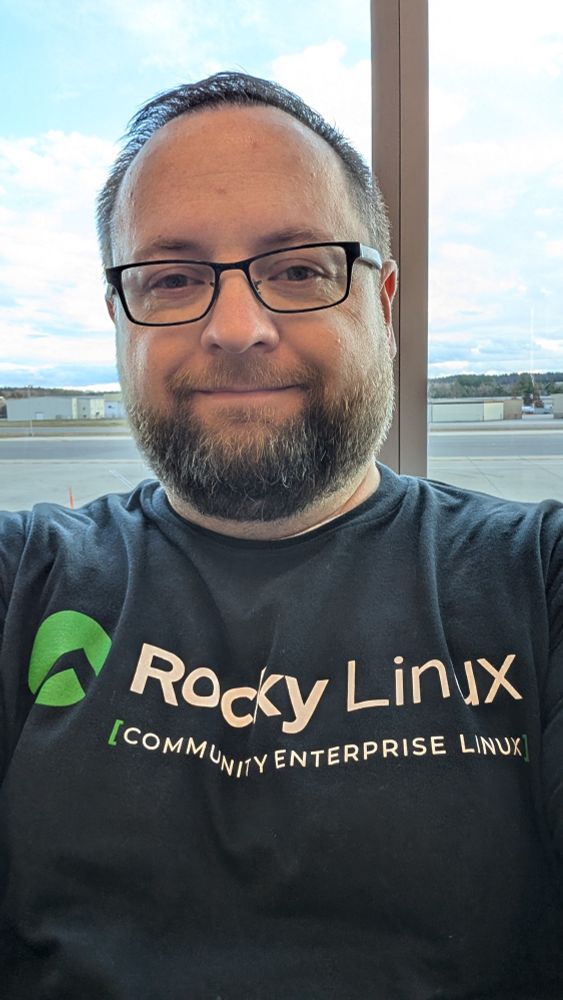 A selfie of Michael Young wearing a Rocky Linux T-Shirt at the airport on his way to SC25 conference in St. Louis, Missouri.