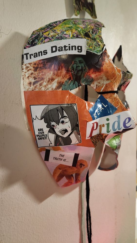 Mask covered in collage with many colour's and textures we see a woman screaming surrounded by flames, a Manga woman with googly eyes with text reading 'are our people safe?' With a block below it reading 'the truth is' next to an image of a primate. We see TRANS DATING in newsprint -- real -- PRIDE (IN RAINBOW)