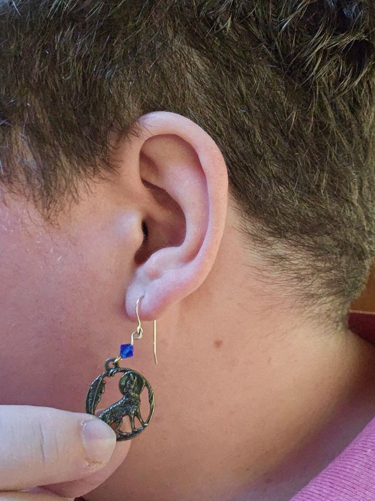 A dangling metal earing, about the size of a quarter, depicting a wolf howling at the moon, hanging from my ear