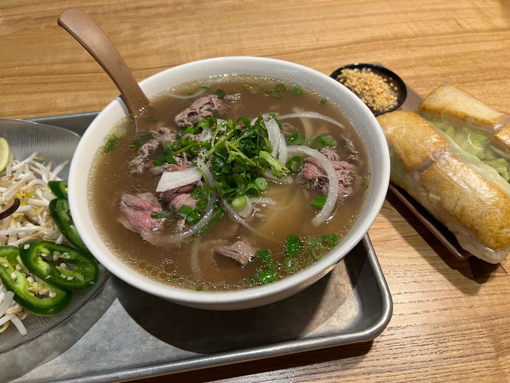 A bowl of beef phō with sprouts and vegetables and two tofu spring rolls on the side.