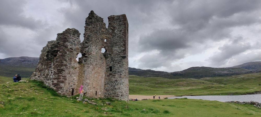 Kuva raunio linnasta edustalla ja taustalla on karua vuoristoista maisemaa sekä tummat pilvet taivaalla