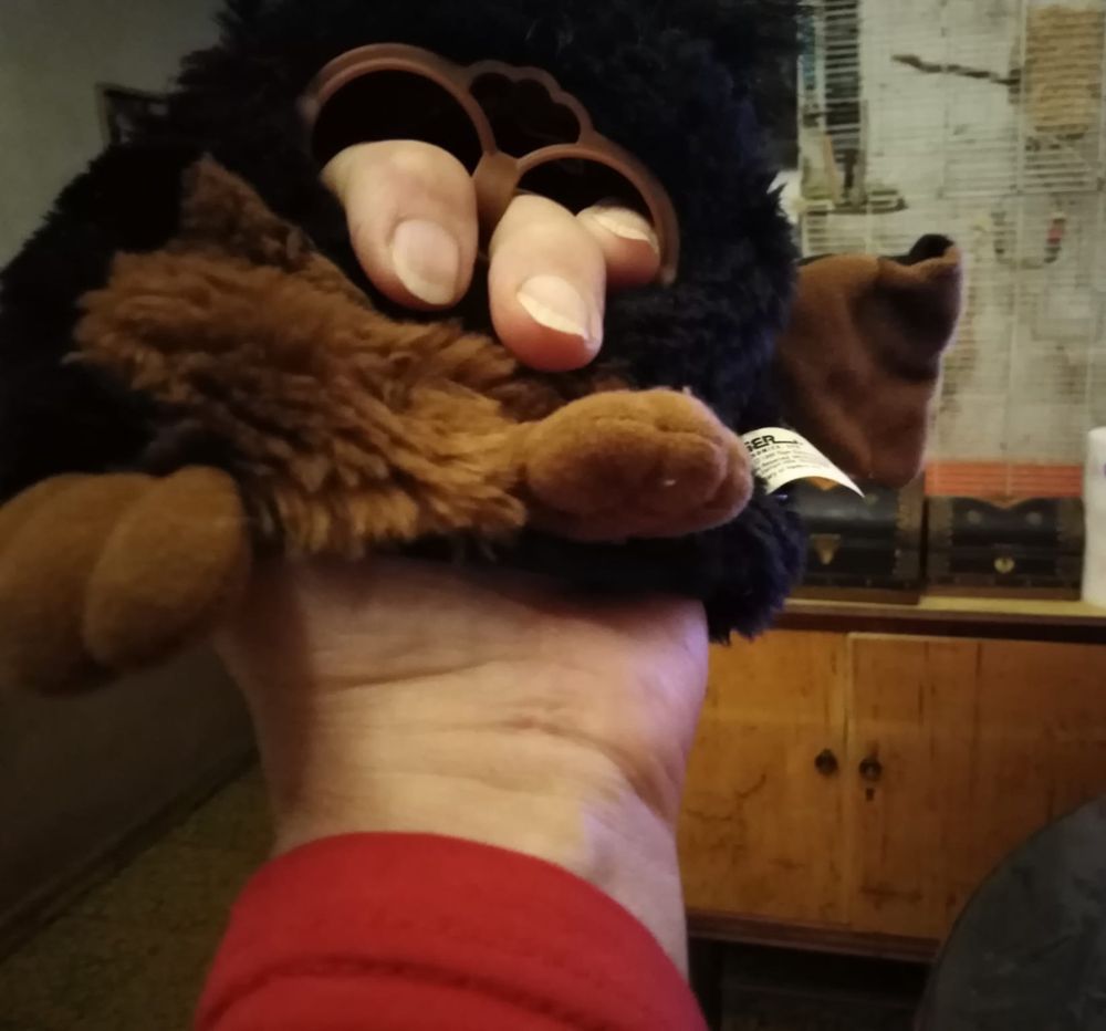 Pellejo de Furby marrón y negro puesto cual títere macabro en la mano de mi madre, sacando los dedos por los agujeros de los ojos.