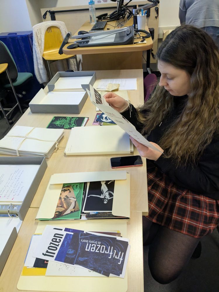 A female student is looking at a leaflet, there are other papers on the table 