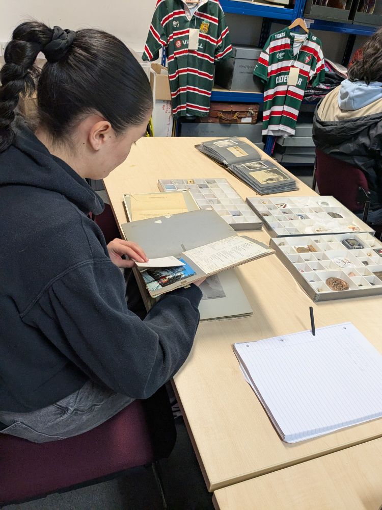A student flicks through some documents, there are papers, a box with small objects and photographic albums on the table