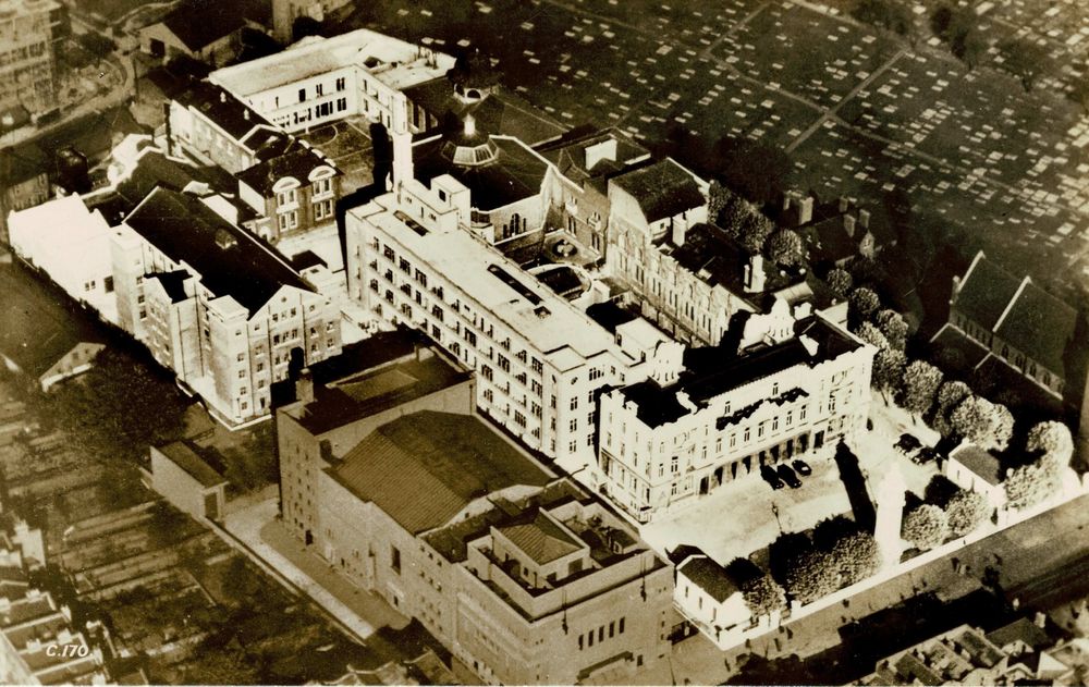 An old monochrome picture postcard showing an aerial view of college buildings set in an urban landscape