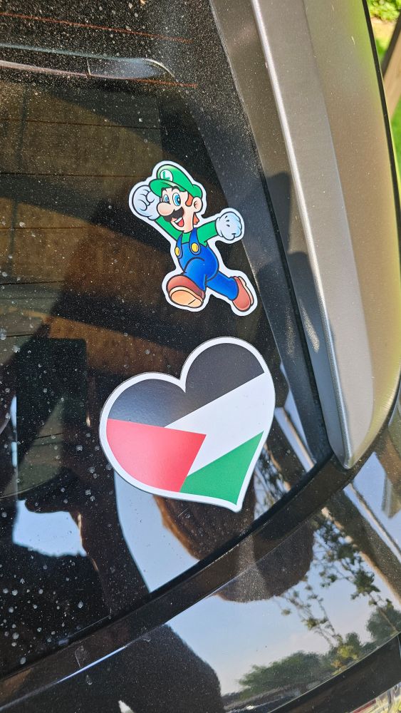 Close up shot of two vinyl decals on a vehicle windshield. One is Luigi (Nintendo) in his signature jumping pose and the other is the Palestinian flag inside of a heart shape. 