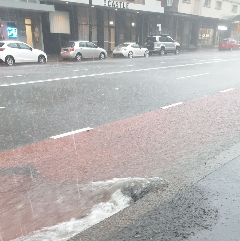 Lots of water on a major road. A large chunk of something in the gutter is restricting water movement.