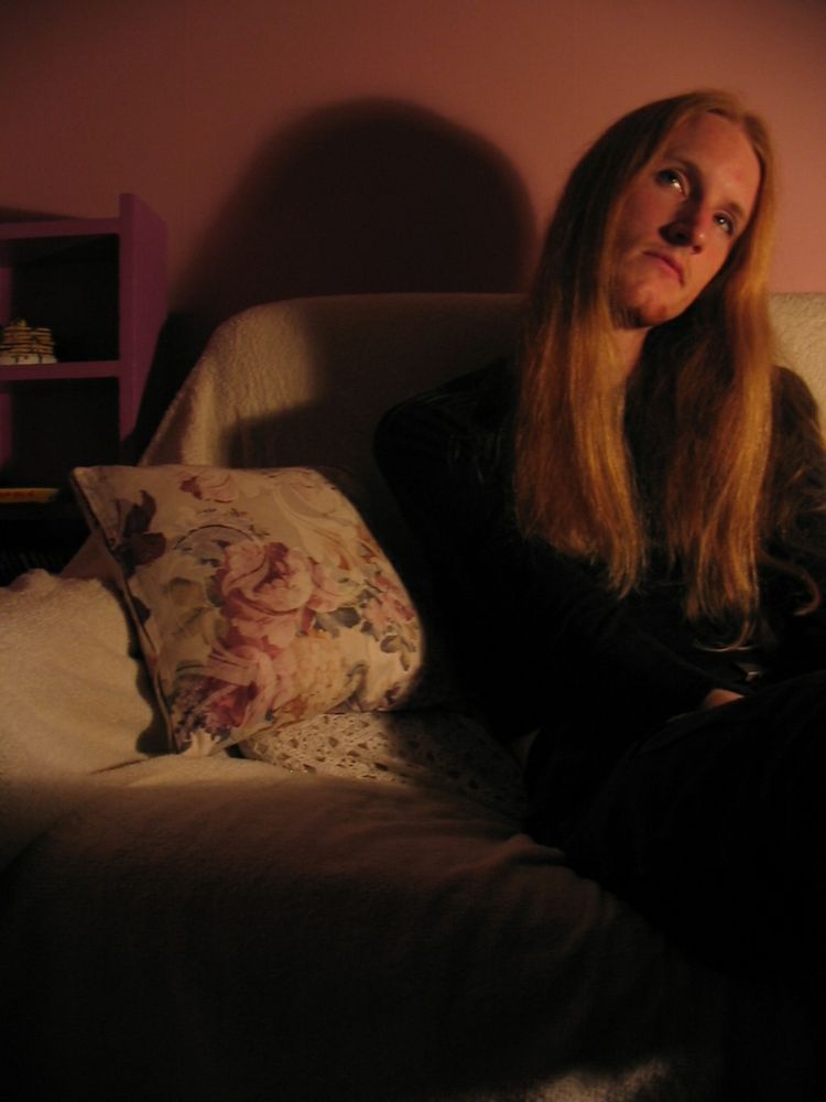 I'm sitting on a couch in a low-lit room. My head is slightly tilted and I'm looking up and off to the side. I have long, straight hair most of the way down to my chest. I didn't smile in photos much back then.
