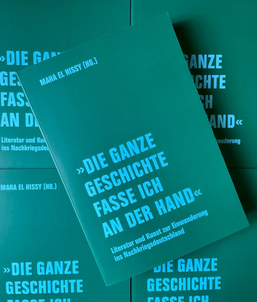 Das Buch, hellblaue Schrift auf grünem Grund, auf weiteren Exemplaren des Buches liegend.