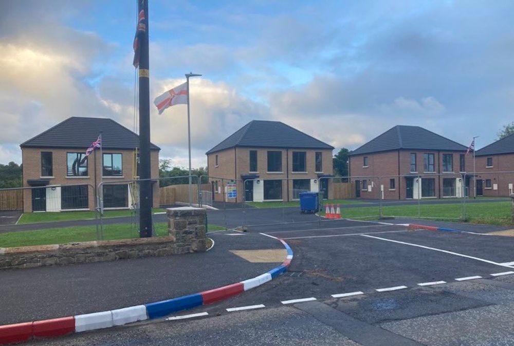 Loyalists erect flags and paint kerbstones in a new mixed housing development in Antrim - 2024.