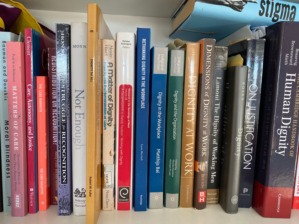 A shelf showing multiple academic books with titles related to dignity at work, recognition, care ethics.