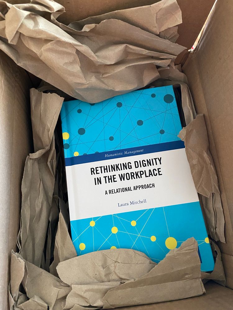 A picture of a blue book titled ‘rethinking dignity in the workplace, a relational approach’ by Laura Mitchell, shown in a cardboard delivery box.
