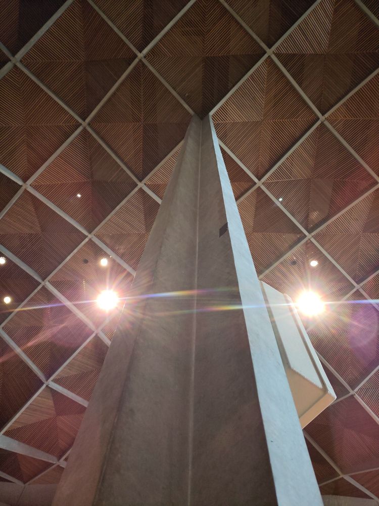 A view up a concrete column towards the square wooden grid of the nave cieling of Coventry cathedral. It's all delightfully modernist