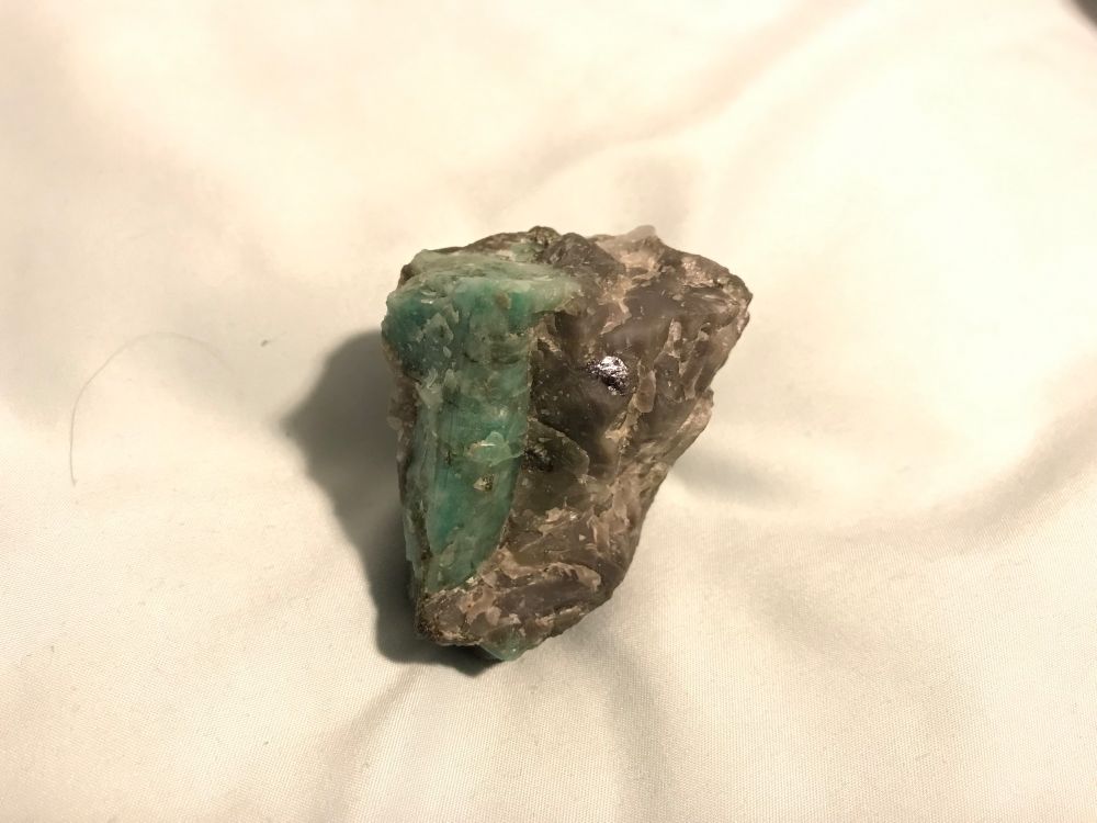 A picture of an opaque green, hexagonal emerald crystal in a greenish gray host rock.