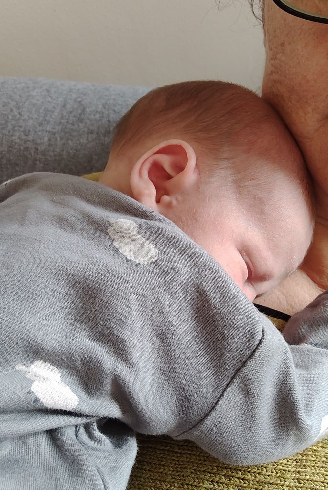 A sleeping baby in a grey sleep suit with a sheep pattern.