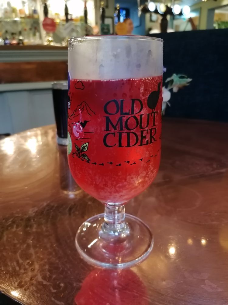 A pint glass full of fruit cider on a copper topped table
