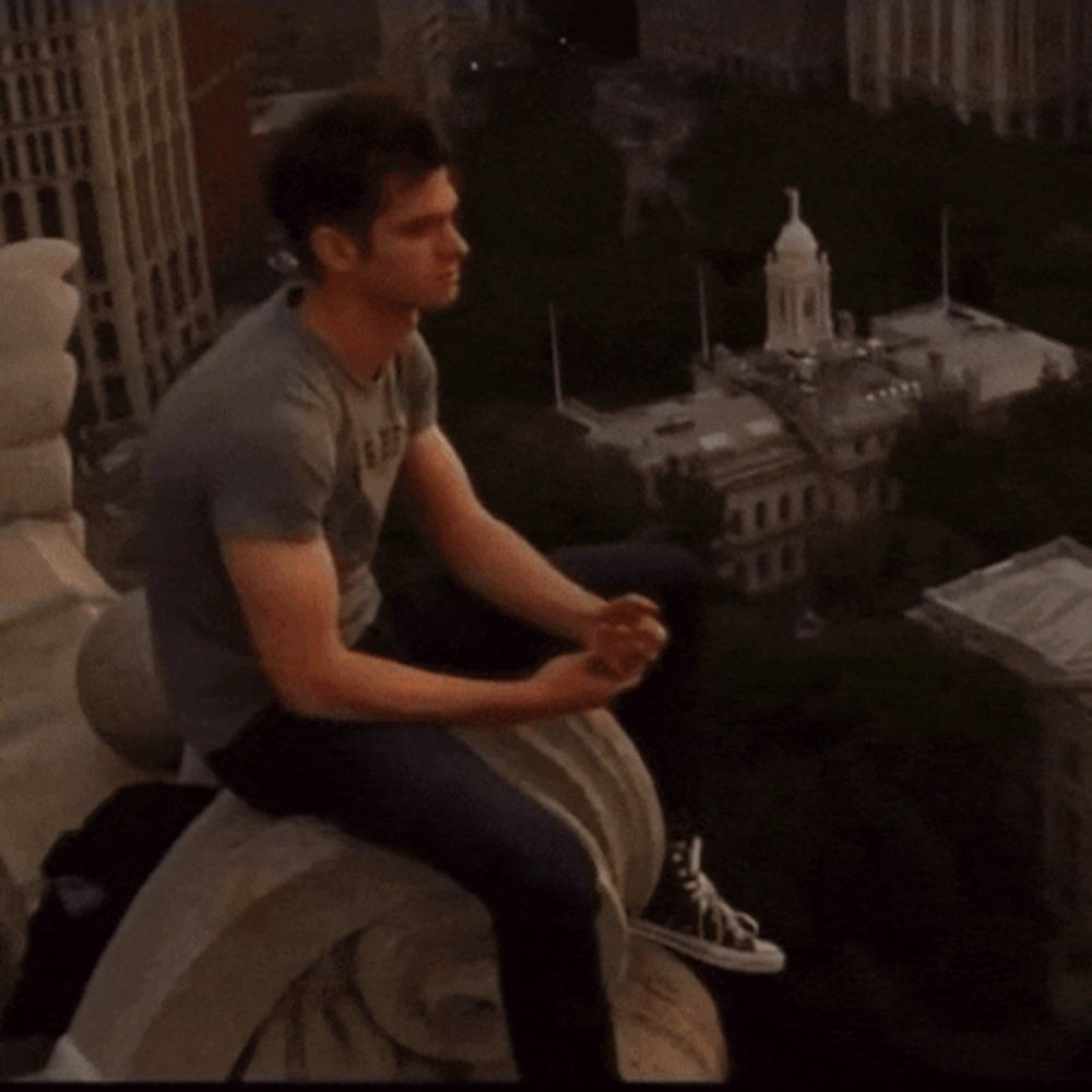 a man sits on a ledge overlooking a city at sunset