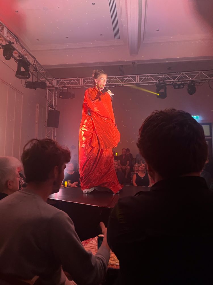 Tall woman in red robe on a round stage surrounded by audience