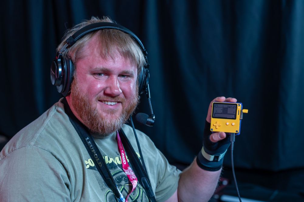 The speedrunner ZeroCounts holding up a yellow Playdate console.