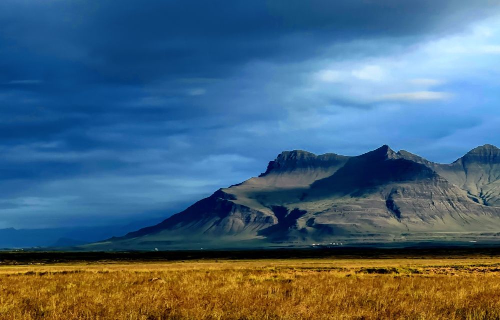 Color image of mountains, a hay field, and dramatic clouds in Iceland.