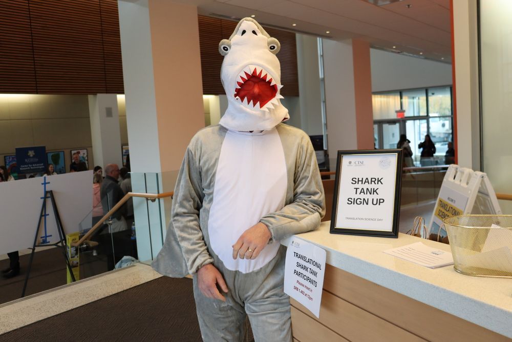 Man in shark costume standing next to sign that says "Shark Tank Sign Up"
